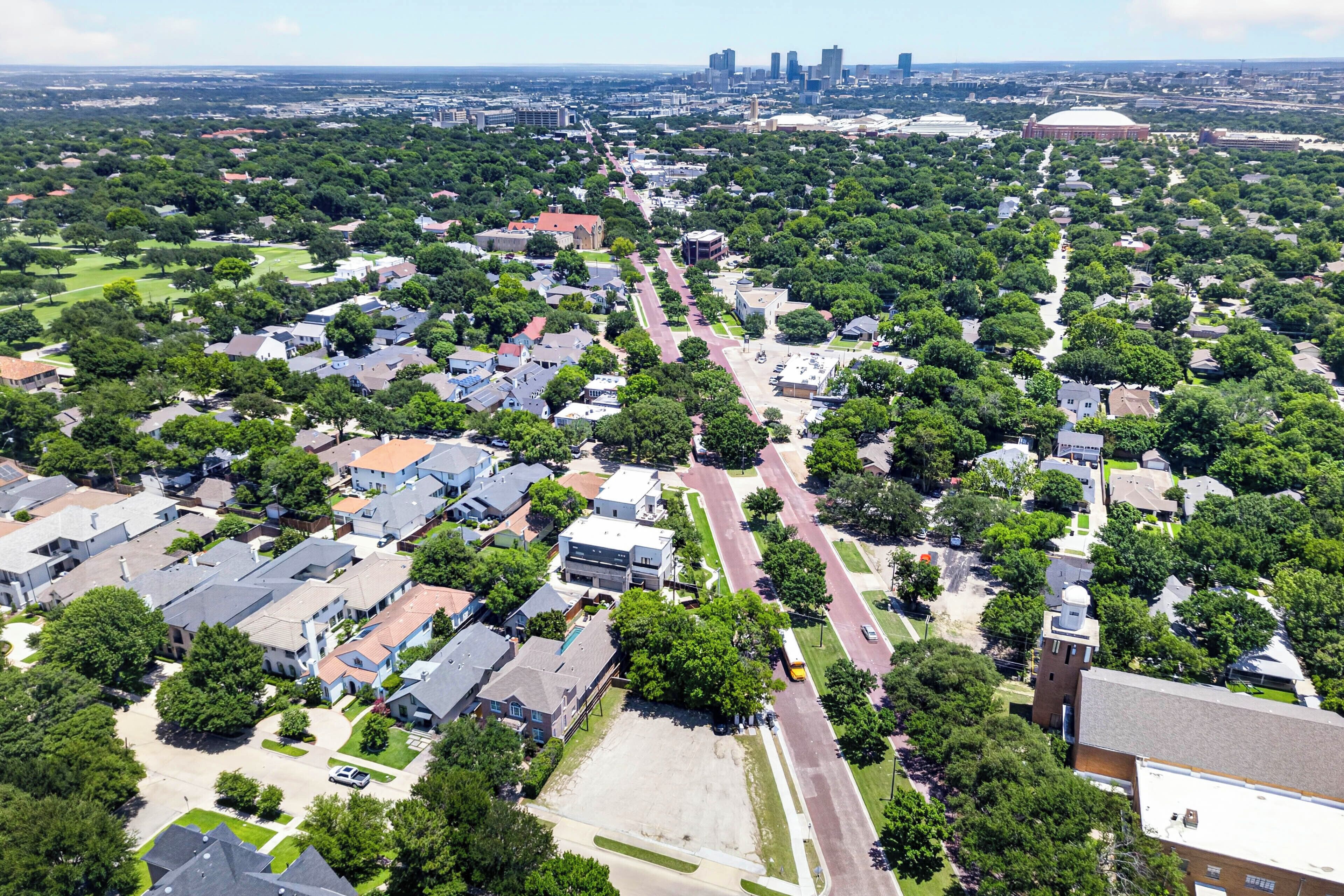 An aerial view of a residential area with houses, streets, and a distant city skyline.