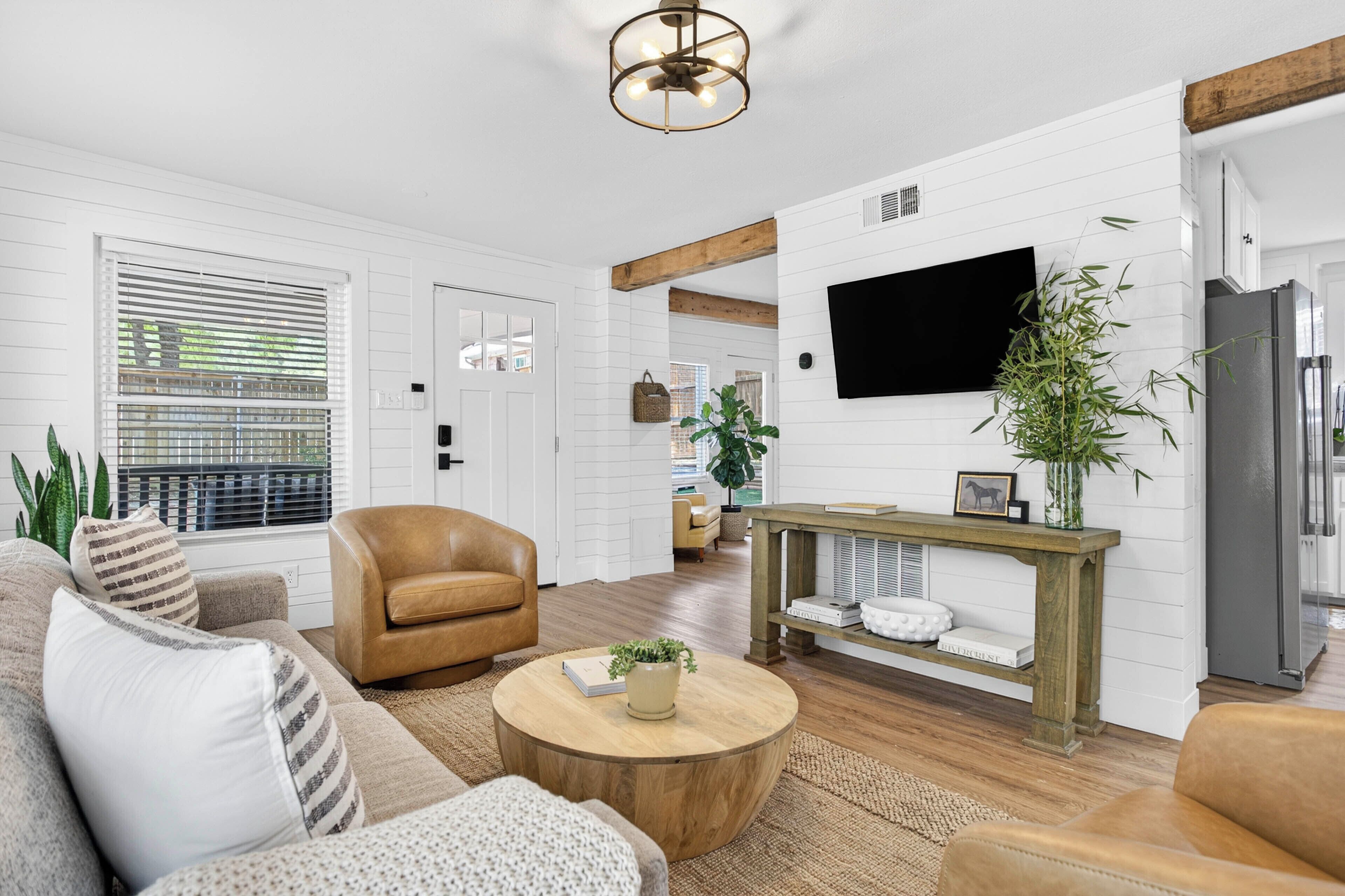 A living room with a sofa, armchair, coffee table, and a TV mounted on the wall.