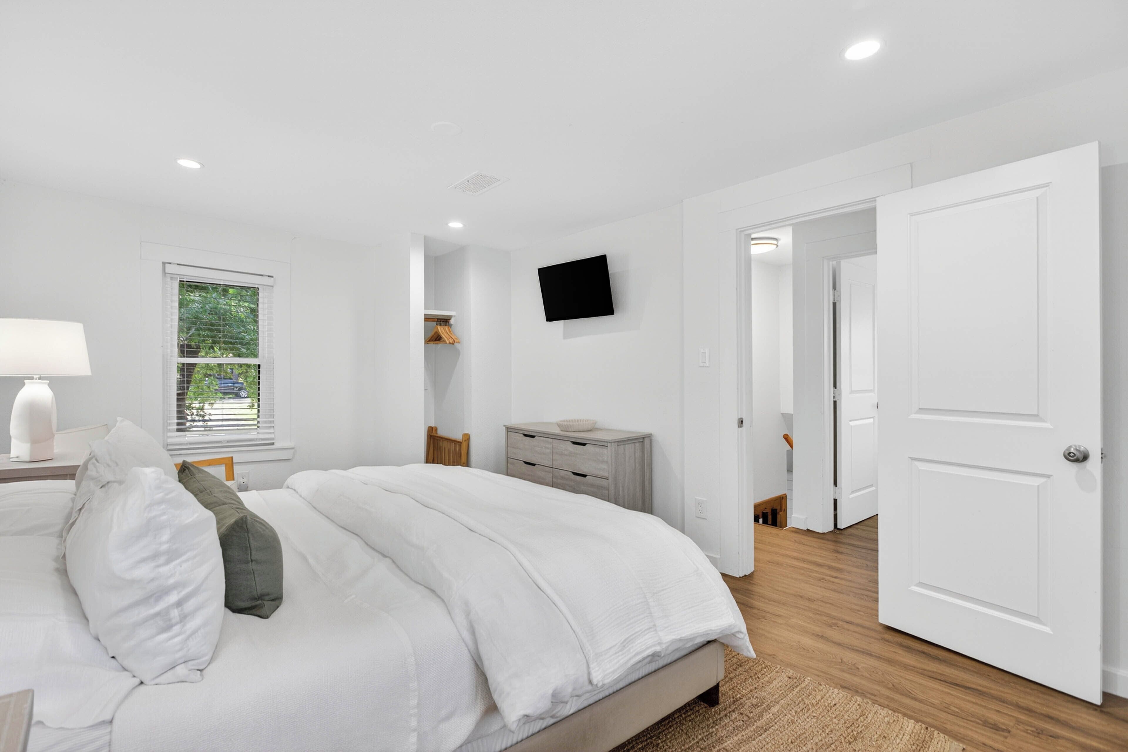 A bedroom with a bed, a TV, a window, and a door.