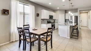 A modern kitchen with white cabinets, a central island, and a dining area with wooden chairs. - Suburban Santa Fe Home Near Main Street & I-25 (Los Lunas)