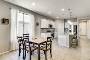 A modern kitchen with white cabinets, a central island, and a dining area with wooden chairs.