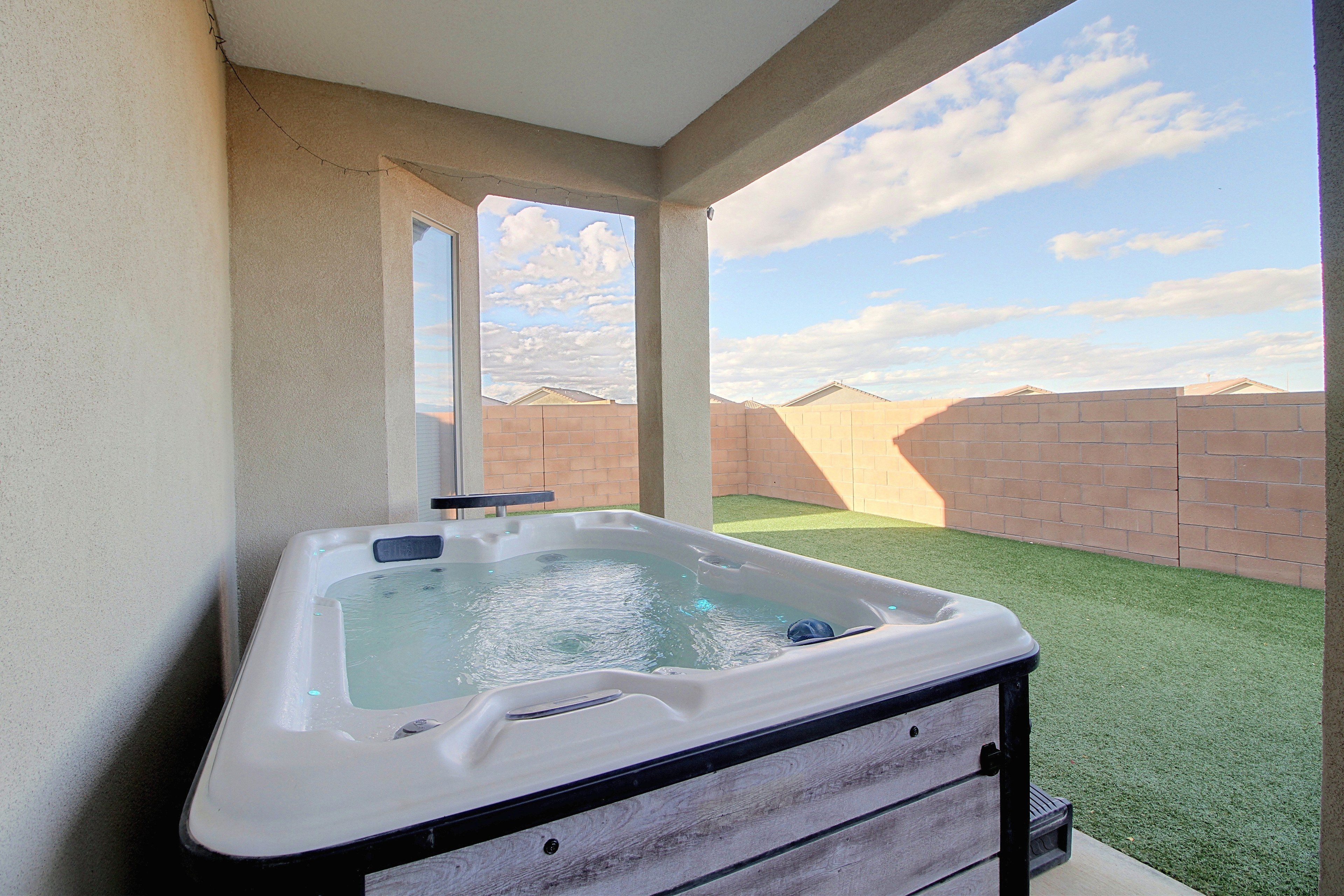 A hot tub in a covered outdoor area with a view of a brick wall and a clear sky.