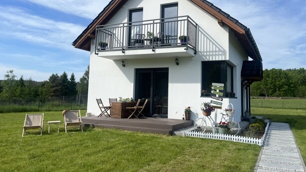 Ein zweistöckiges Haus mit Balkon, Veranda und weißem Zaun.