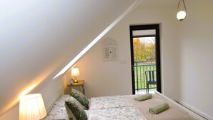 Ein Schlafzimmer mit Bett, Nachttisch mit Lampe, Fenster mit Blick ins Freie und einer Tür.