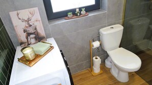 Ein Badezimmer mit Toilette, Fenster, Waschbecken mit Handtuch, Kerze und einer kleinen Pflanze.