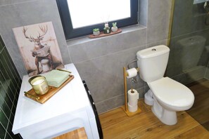 Ein Badezimmer mit Toilette, Fenster, Waschbecken mit Handtuch, Kerze und einer kleinen Pflanze.