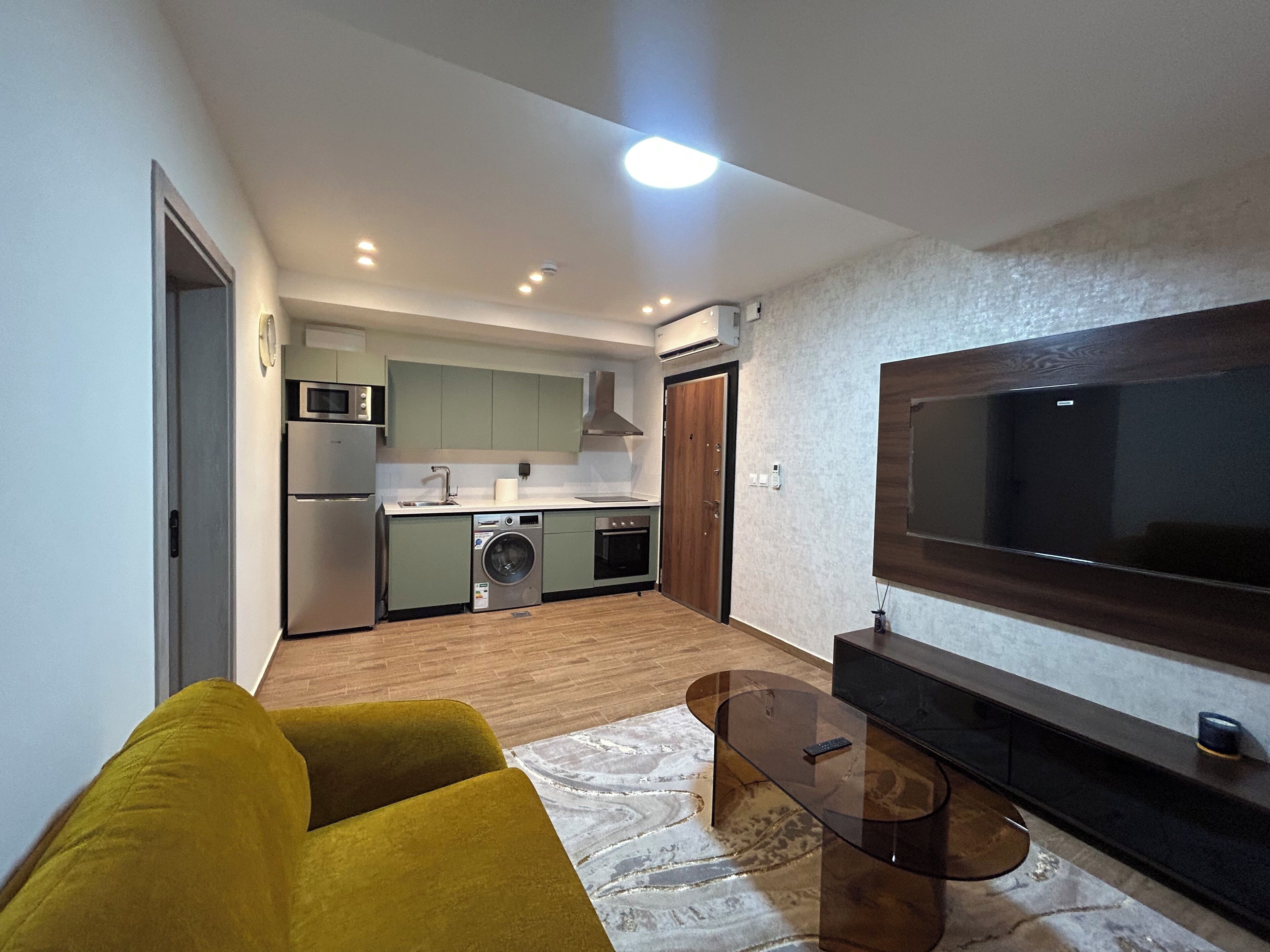 A compact living space with a kitchenette, a sofa, a TV, and a glass coffee table.