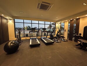 Una palestra con tapis roulant, ellittiche e vogatore, con ampie finestre che offrono vista all'esterno.