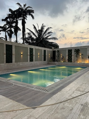 Una piscina con solárium de baldosas, rodeada de muros con iluminación integrada y vegetación.