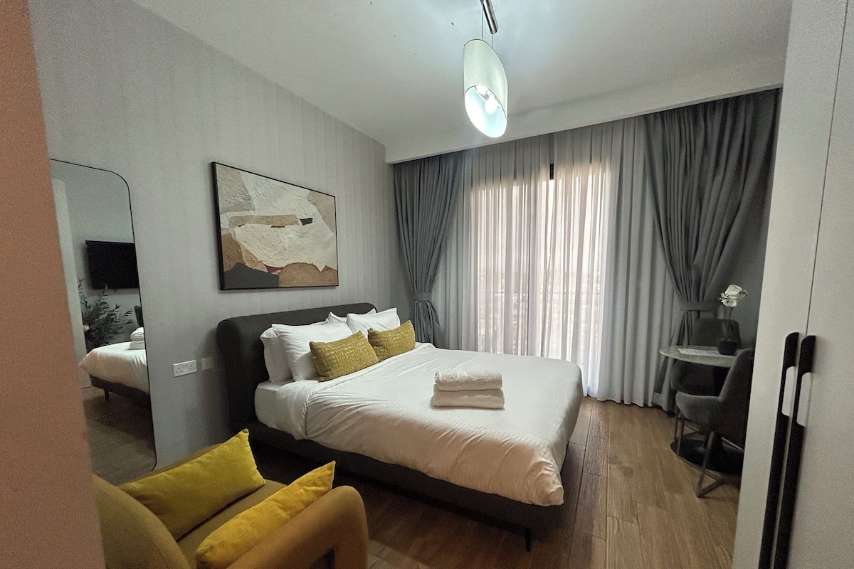 Quarto de hotel com cama, escrivaninha, cadeira, televisão e um quadro na parede.