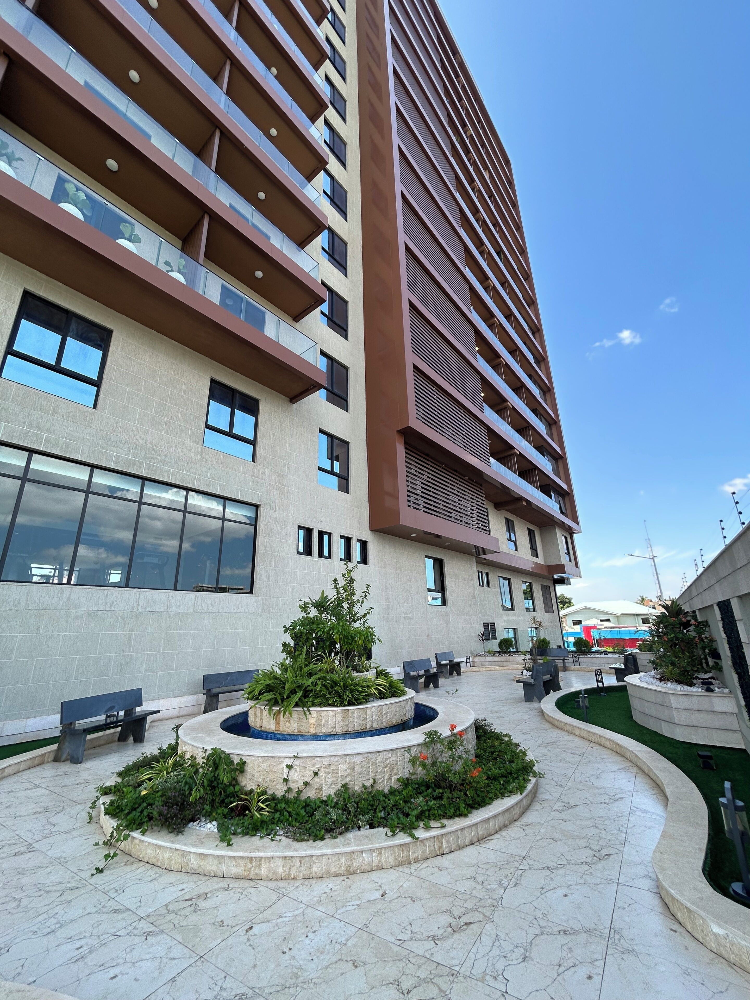 A modern building with multiple floors, large windows, and a courtyard with seating and greenery.