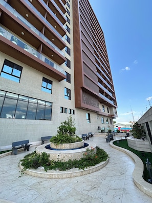 Un edificio moderno de varios pisos, con amplias ventanas y un patio con asientos y vegetación.