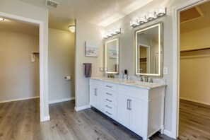 A bathroom with a white vanity, large mirrors, and a wooden floor. - Near The Woodlands! Group Retreat w/ Yard & Patio (Spring)