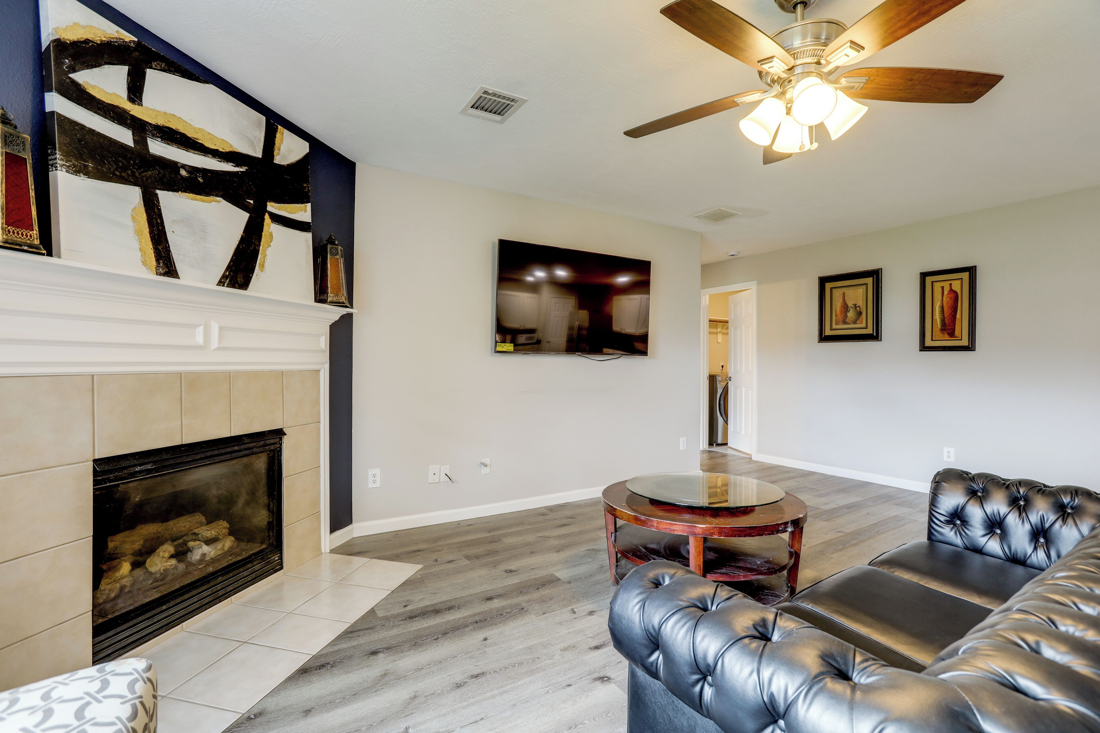 A living room with a fireplace, leather sofa, round coffee table, and a ceiling fan.
