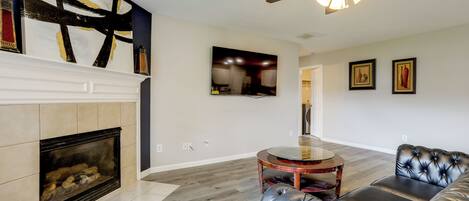 A living room with a fireplace, leather sofa, round coffee table, and a ceiling fan.