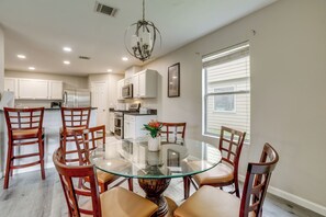 A dining area with a glass table surrounded by wooden chairs, a chandelier, and a kitchen in the background. - Near The Woodlands! Group Retreat w/ Yard & Patio (Spring)