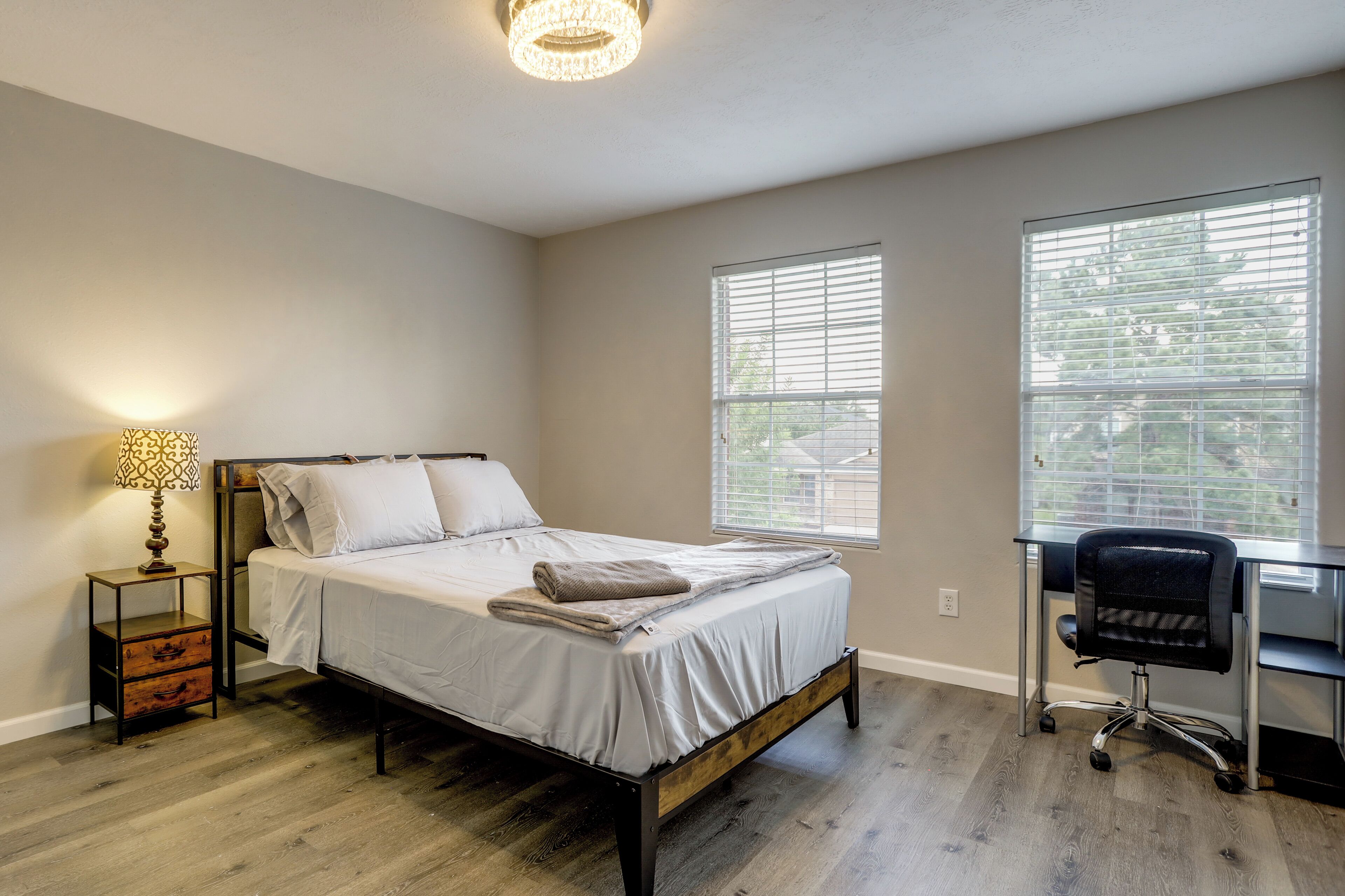 A bedroom with a bed, bedside table, lamp, and a desk with a chair.