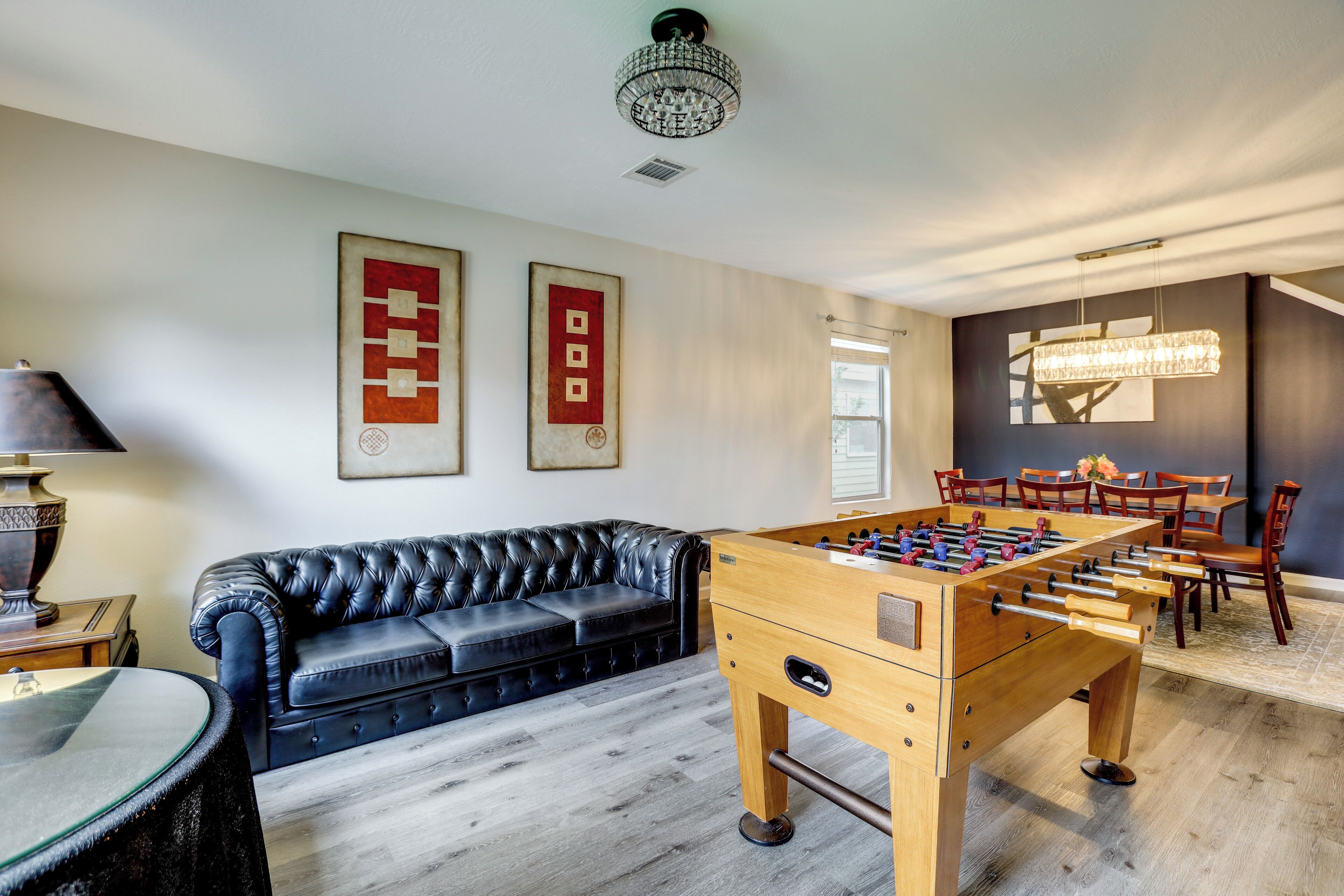 Una habitación con mesa de fútbol, sofá de cuero y comedor con sillas y candelabro.