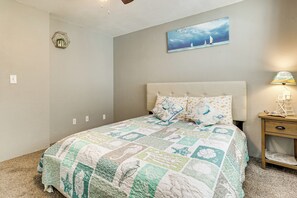 A bedroom with a large bed, a nightstand, a wall-mounted lamp, and a painting of sailboats. - Centrally Located! Brand New South Daytona Retreat (Daytona Beach)