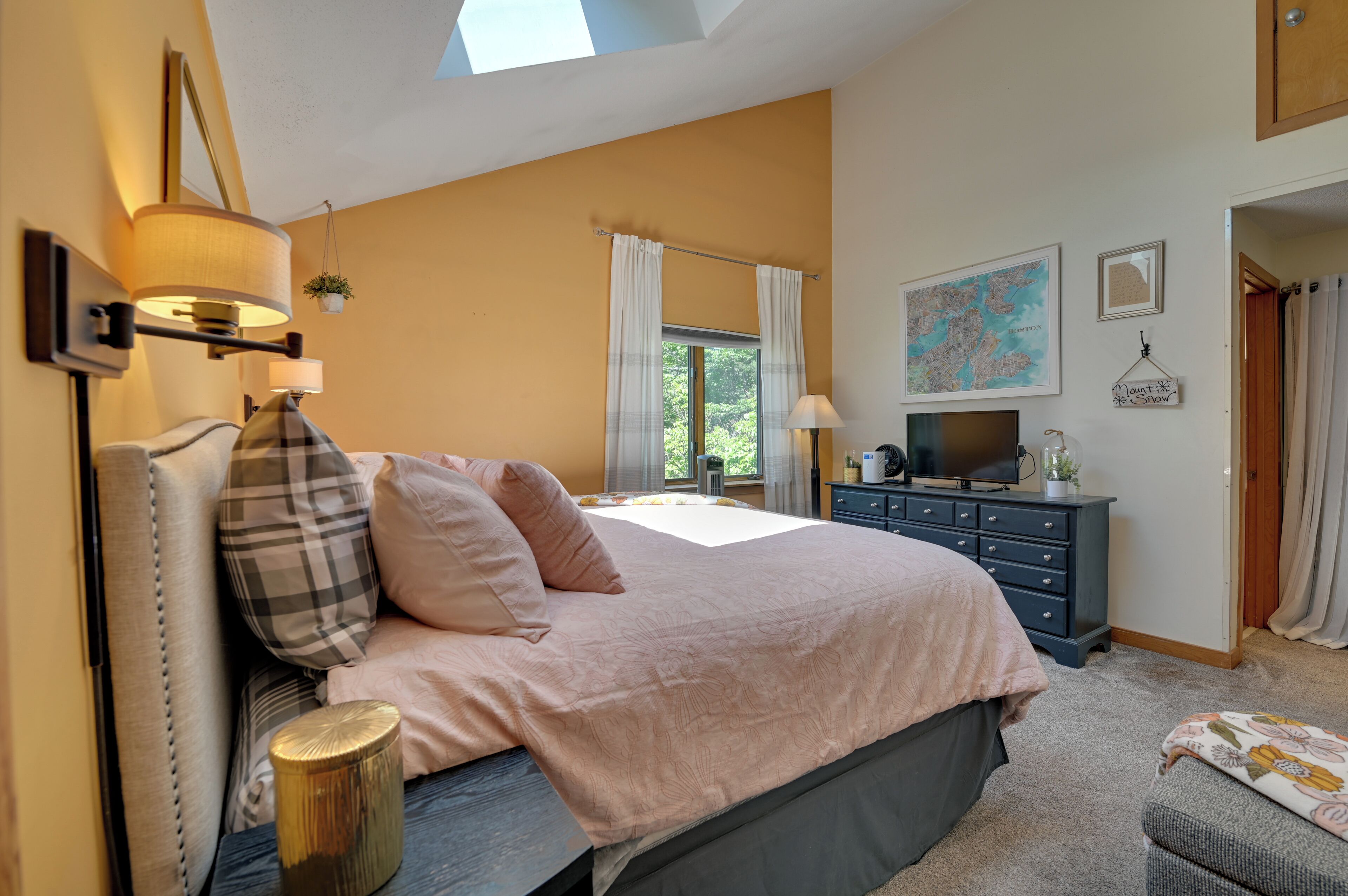 A bedroom with a bed, bedside lamps, a dresser, a television, and a window with curtains.
