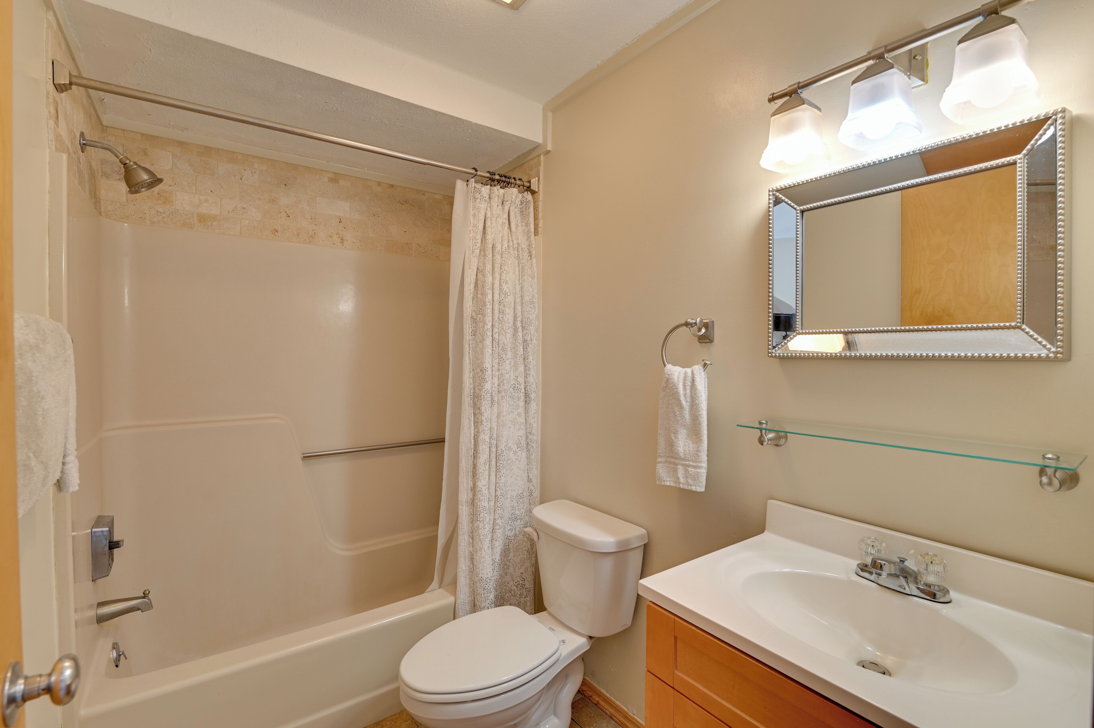 A bathroom with a bathtub, toilet, sink, and a mirror with lights.