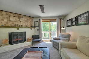 A living room with a fireplace, a sofa, a chair, and a balcony with a view of trees. - Hike, Bike & Ski! Condo Steps to Mount Snow Resort (West Dover)