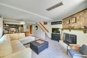 A living room with a sofa, ottoman, fireplace, television, and kitchen in the background. - Hike, Bike & Ski! Condo Steps to Mount Snow Resort (West Dover)