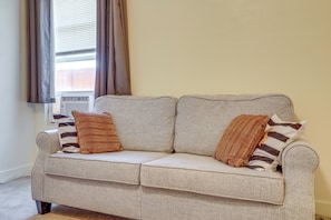 A light-colored sofa with two striped pillows, positioned near a window with curtains.