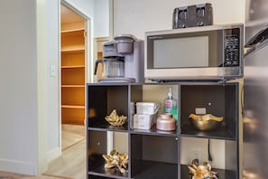 Une petite cuisine équipée d’une machine à café, d’un four à micro-ondes et d’étagères où sont disposés des objets décoratifs.