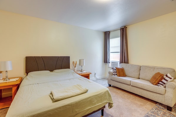 A hotel room with a bed, a sofa, a nightstand with lamps, and a window with curtains.
