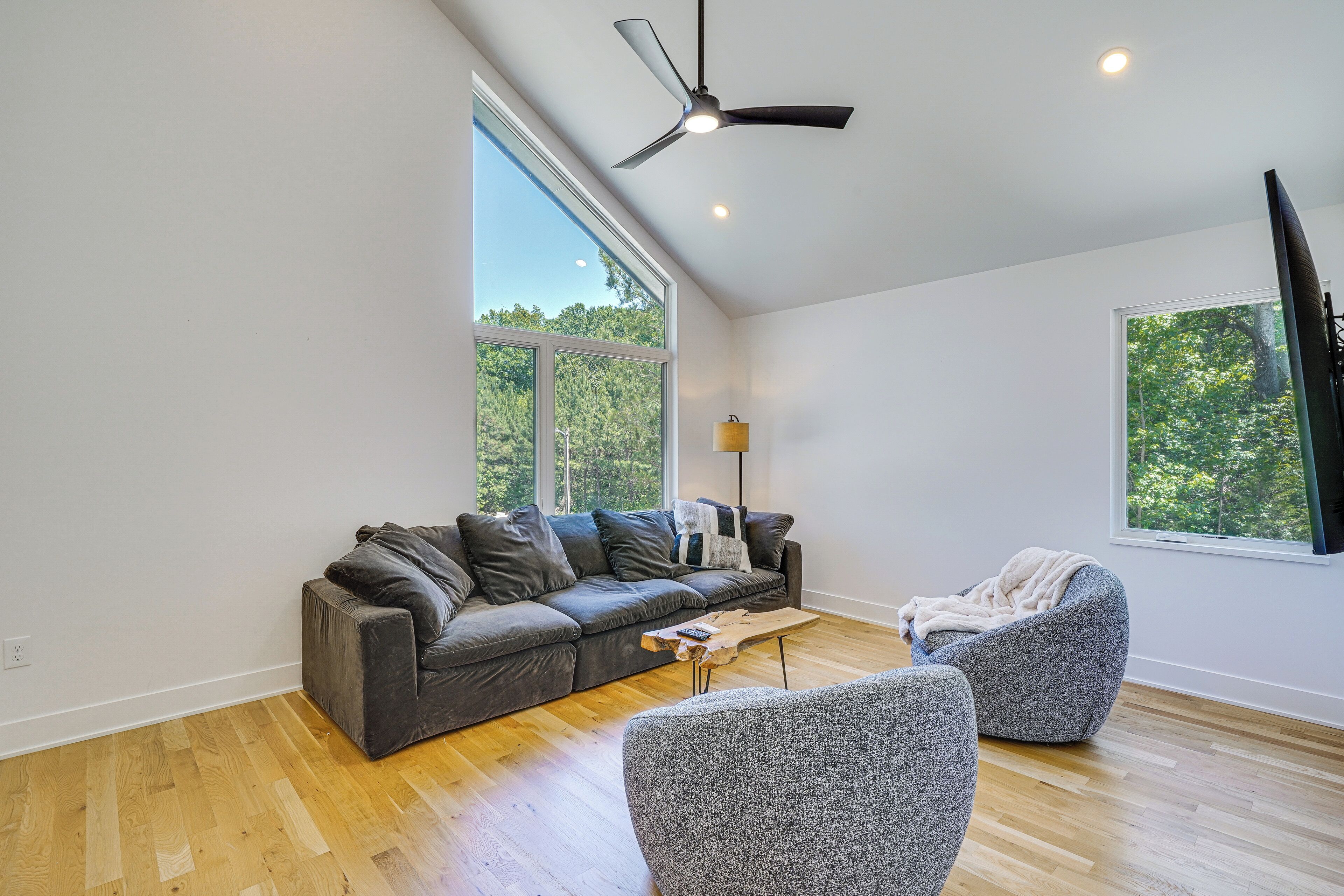 A modern living room with a grey sofa, a grey armchair, a wooden coffee table, and a ceiling fan.