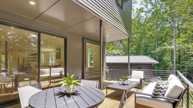 Eine moderne Terrasse im Freien mit rundem Tisch, Stühlen, einer Couch und Kübelpflanzen.