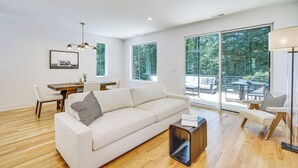 Ein modernes Wohnzimmer mit Sofa, Esstisch und Stühlen, großen Fenstern und Blick ins Freie.