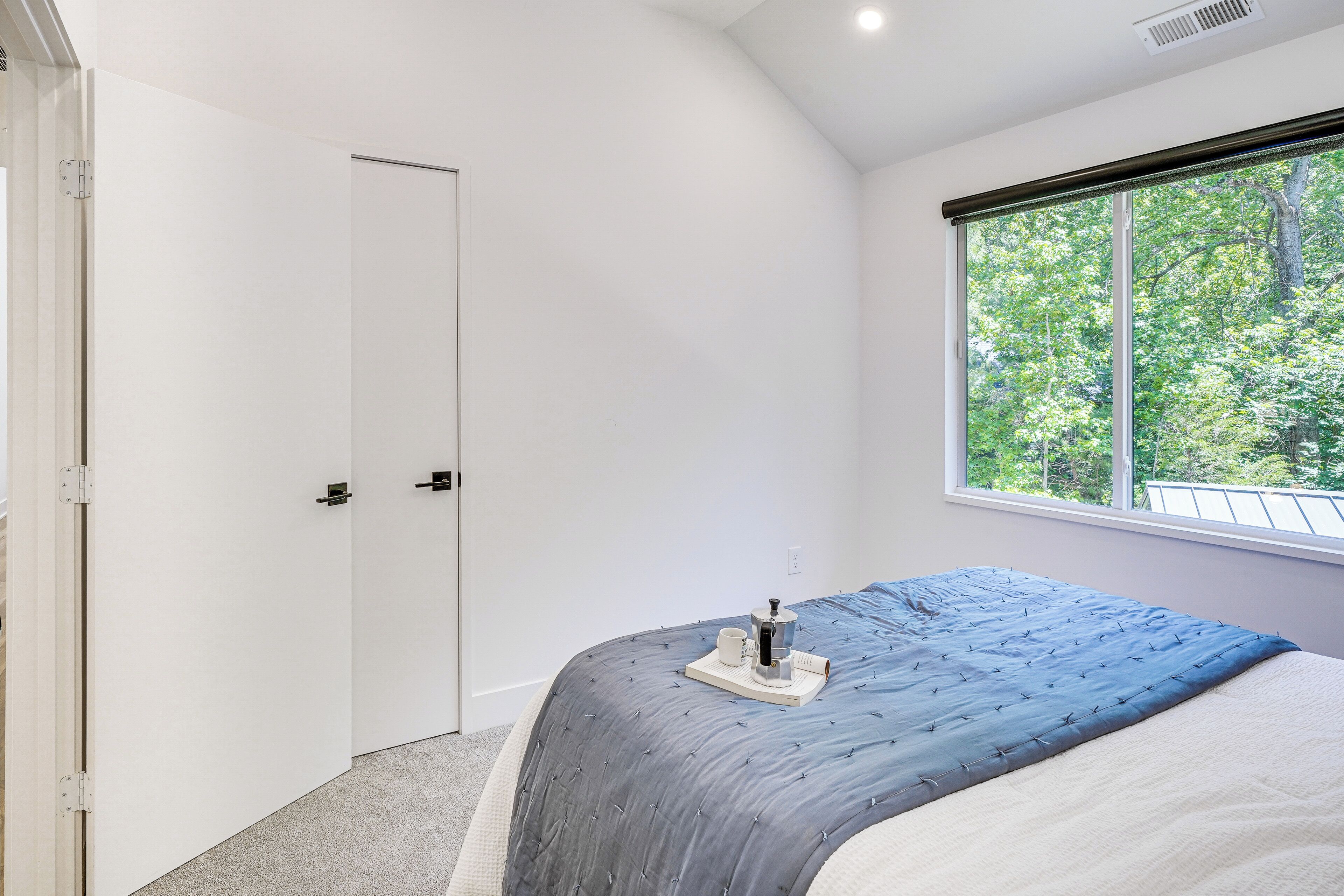 A bedroom with a bed, a window with a view of trees, and a door.