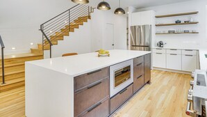 Eine moderne Küche mit einer zentralen Kochinsel, einer Holztreppe und integrierten Geräten.