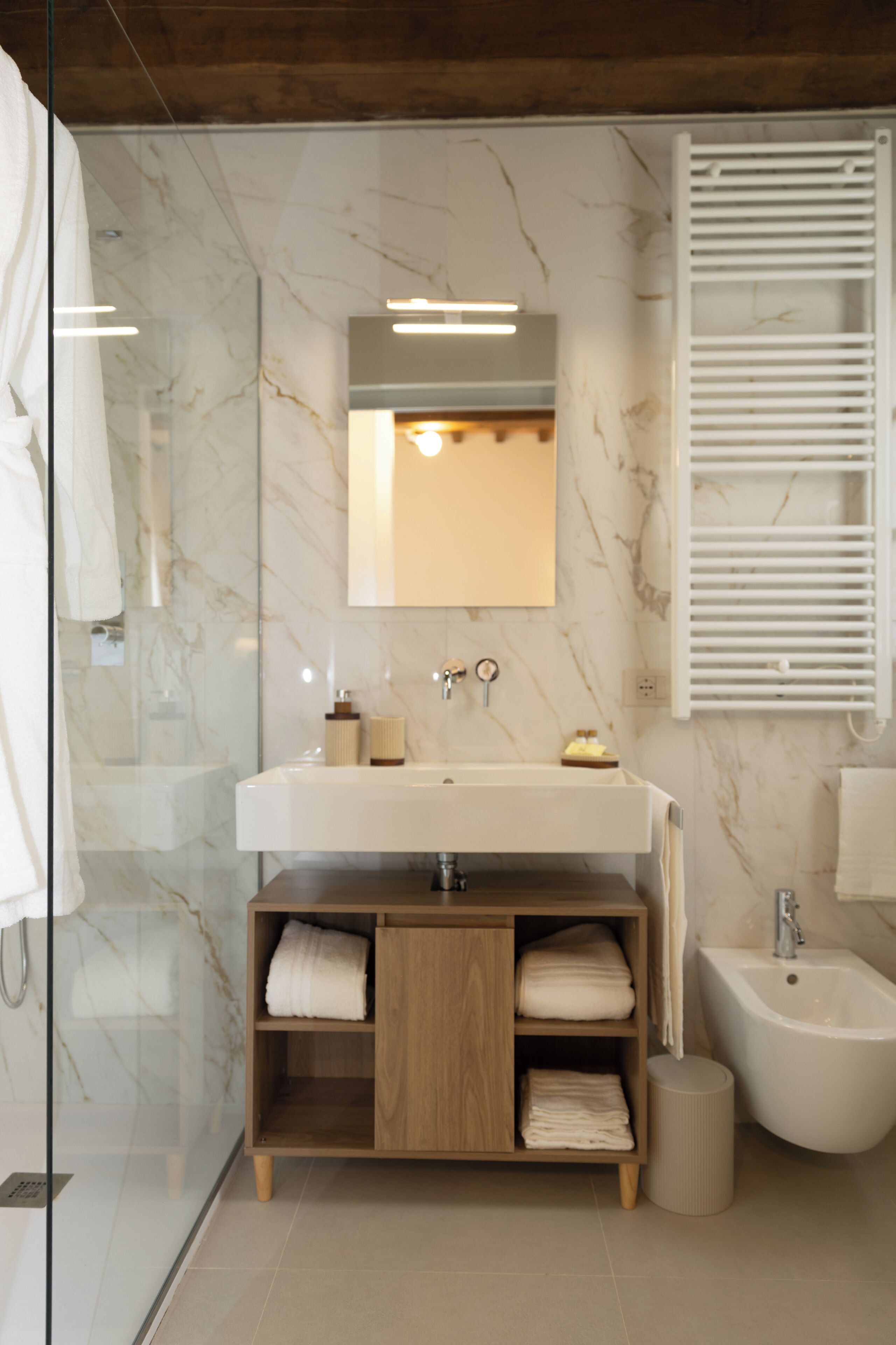 Un bagno moderno con una parete in marmo, un mobile bagno in legno, un bidet e una cabina doccia in vetro.