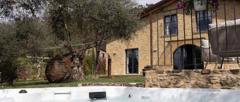 A hot tub in front of a stone building with a chair and a potted plant.