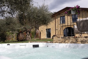 Un bain à remous se trouve devant un bâtiment en pierre, avec une chaise et un pot de fleurs.