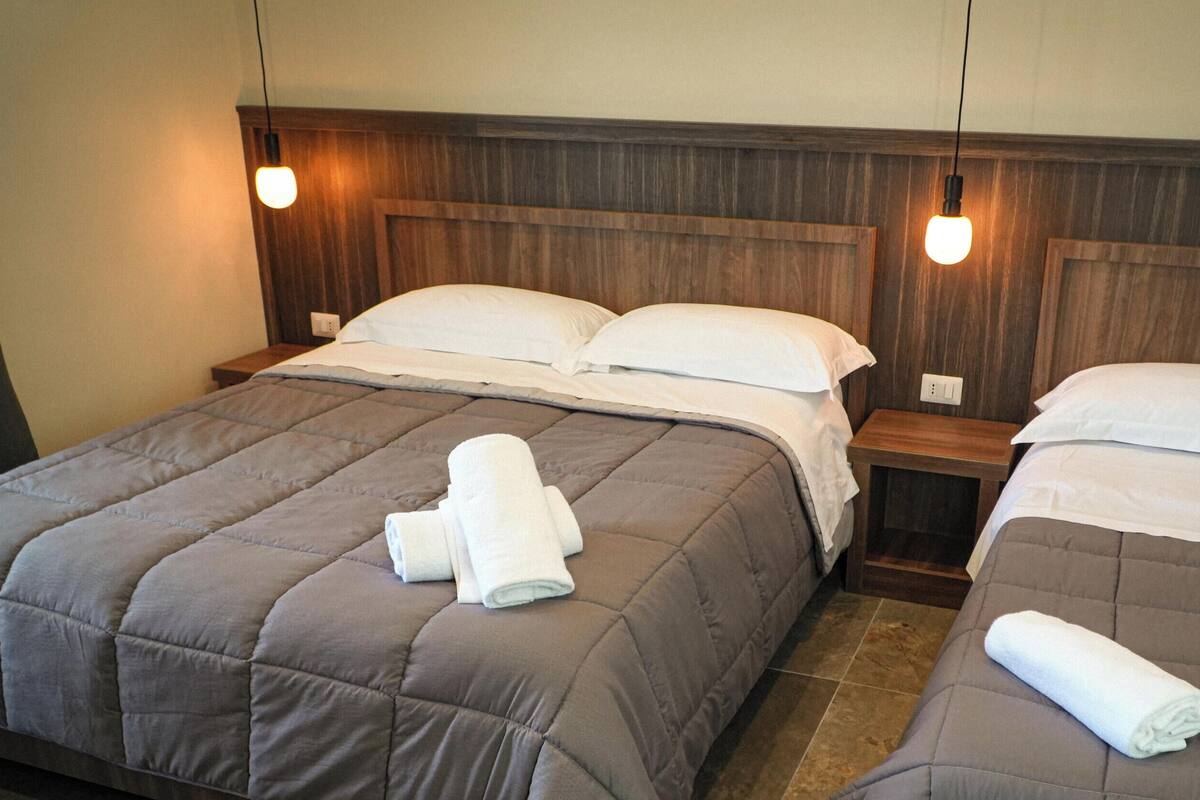 A hotel room with two beds, each with a wooden headboard, and a small bedside table.