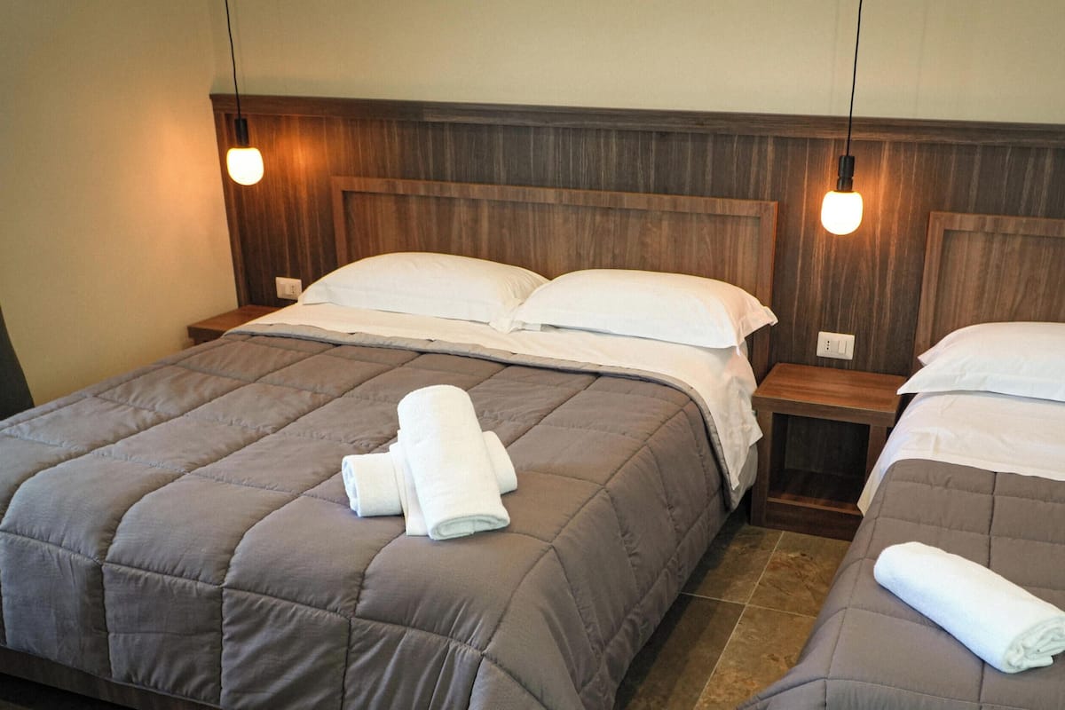 Hotellihuone, jossa on kaksi sänkyä, joissa kummassakin on puinen pääty, sekä pieni yöpöytä.