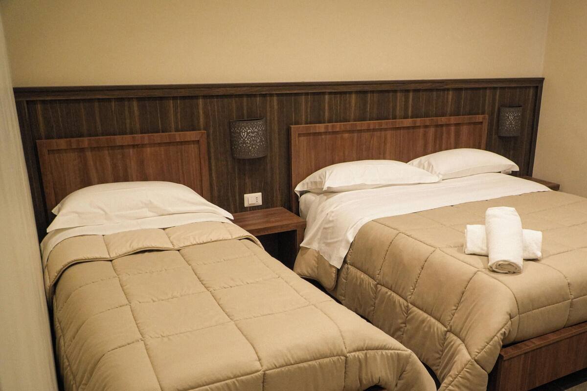 A hotel room with two beds, wooden headboards, and a nightstand with a lamp.