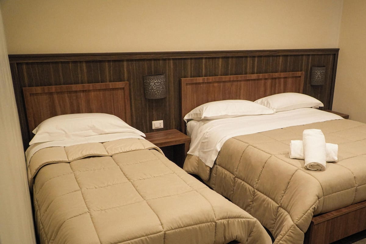 Hotellihuone, jossa on kaksi sänkyä, puiset päätylevyt ja yöpöytä, jossa on lamppu.