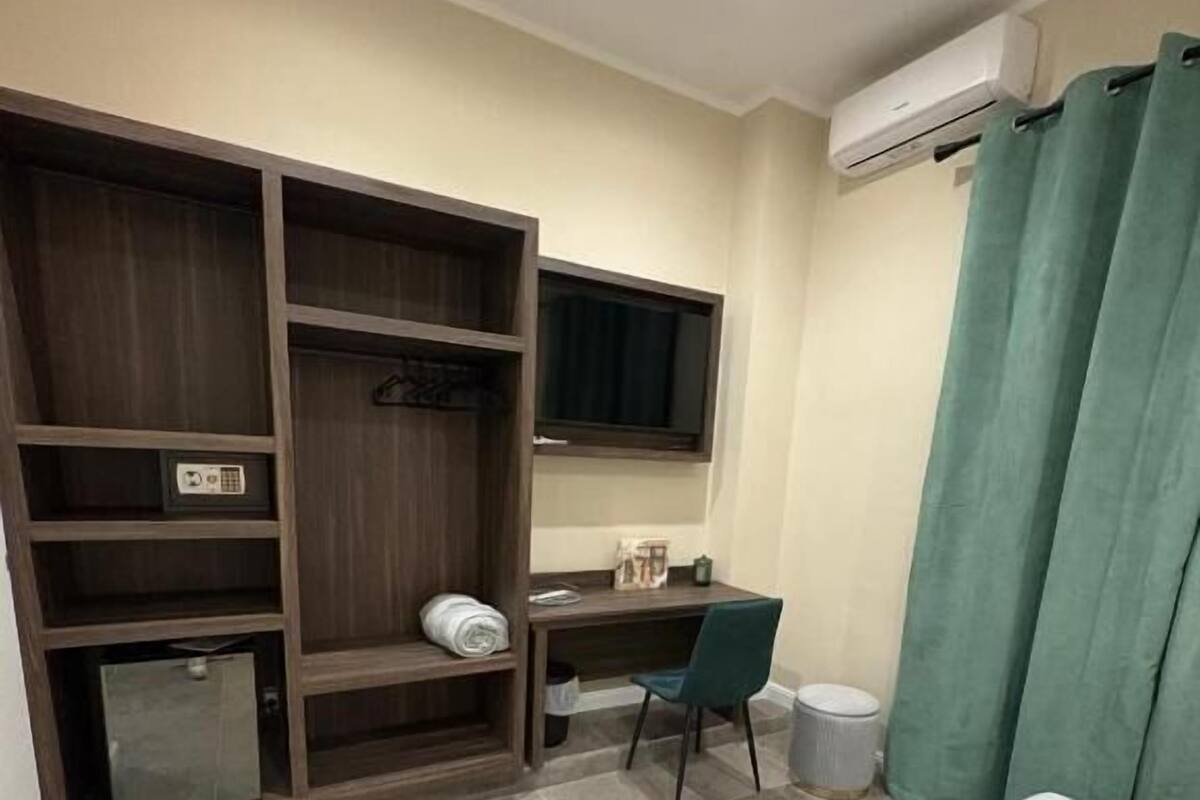 A hotel room with a bed, a desk, a chair, a wardrobe, and a small trash bin.