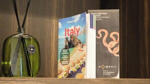 Eine Minibar mit einer grünen Flasche, einem Buch mit dem Titel 'Italien' und einer Broschüre für den 'Archäologischen Park Pompeji'.