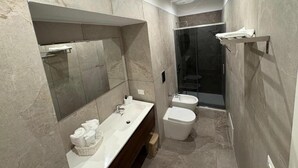 Ein modernes Badezimmer mit einem großen Spiegel, einem Waschbecken, einem Bidet und einer Duschkabine.
