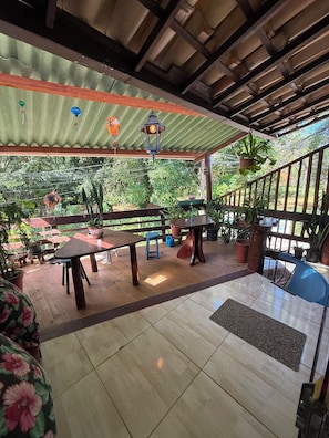 A covered outdoor patio with wooden tables and benches, potted plants, and a view of greenery. - Arandú Hostel (Itacaré)