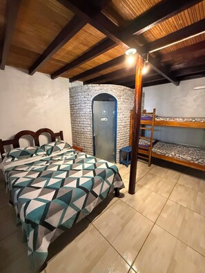 Quarto com cama, beliche, parede de pedra e porta.
