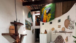 Un pasillo estrecho con piso de baldosas, una mesa de madera con una cesta tejida, un refrigerador blanco y un cuadro colorido en la pared.