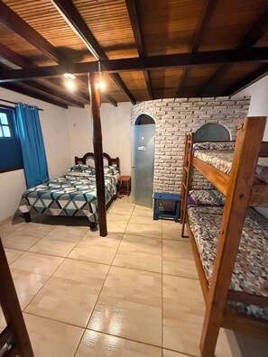 Quarto com cama de solteiro, beliche, parede de tijolos, porta e janela com cortinas.