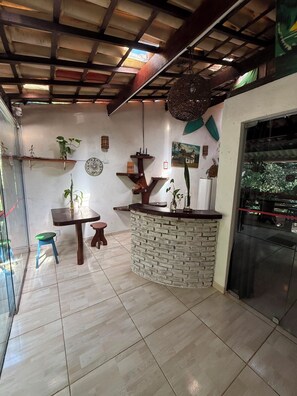 A room with a stone counter, wooden ceiling beams, and a glass door leading outside. - Arandú Hostel (Itacaré)